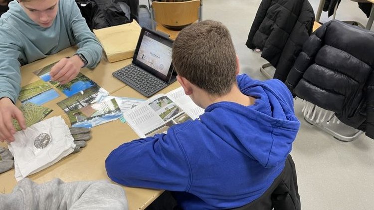 Schüler und Schülerinnen sitzen an Gruppentischen. Mit unterschiedlichen Materialien wie Fotos und Flyern erarbeiten sie die Aufgaben des Volksbundes